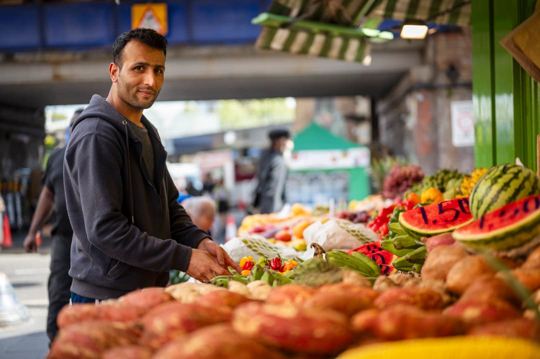 Image of a man working on his fruit stall, smiling at the camera.