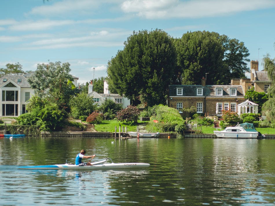 Image of a person rowing a canal boat past some houses.