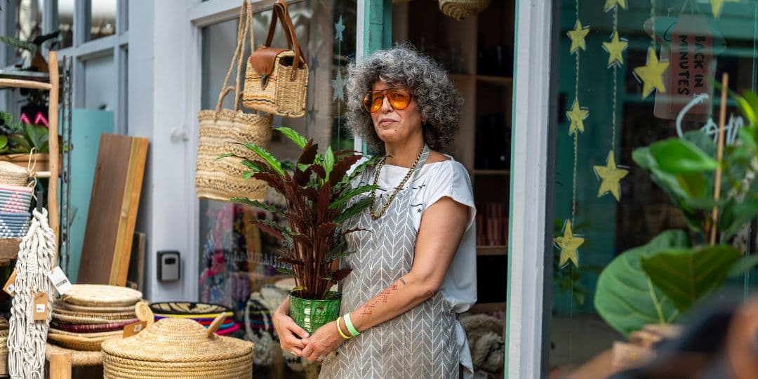 Image of a woman holding a plant, standing outside the front door of her homeware shop.