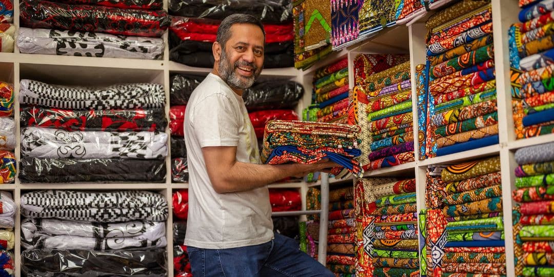 Image of a man on a ladder holding materials, working in his fabric shop.