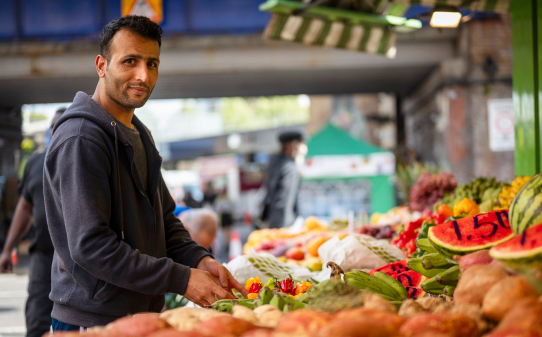 Image of a man working on his fruit stall, smiling at the camera.