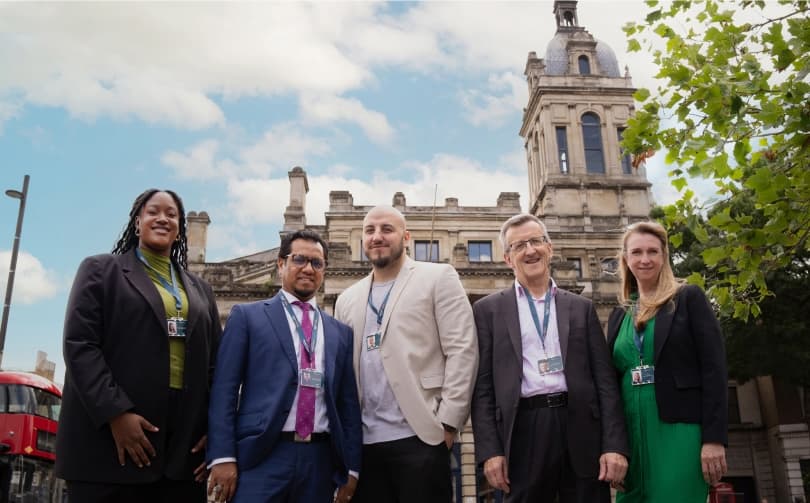 A diverse professional team posing in front of a historic building.